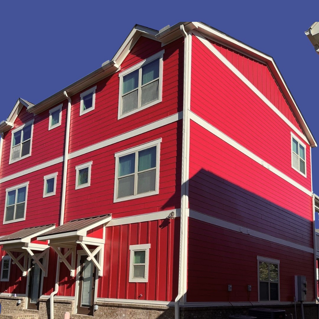 A bright red three-story house with white trim, multiple windows, and a remodeled covered entryway stands against a clear blue sky.